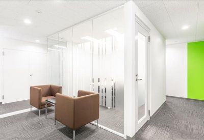Bright communal lounge area with brown armchairs and a glass partition wall.