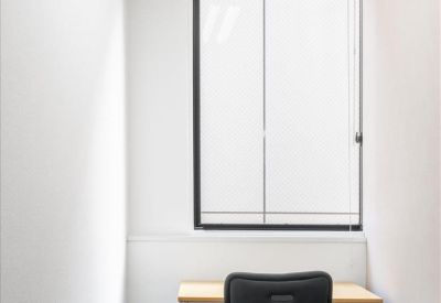 Single-person private office with a black chair and wooden desk by a window.