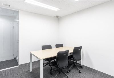 Small meeting room with a light wood table and four black ergonomic chairs.