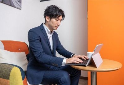 Professional in a suit working on a laptop in a vibrant communal lounge with orange walls.