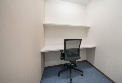 Private windowless office pod with white desk and black mesh chair.