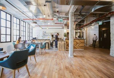 Spacious communal lounge with industrial ceilings, wooden floors, and large windows.