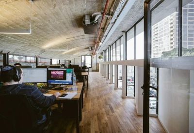 Open-plan office space with long wooden desks and views of a neighboring high-rise.
