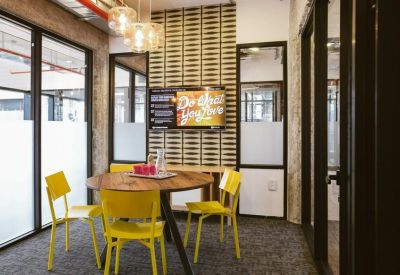 Meeting room with a round wooden table, bright yellow chairs, and a geometric accent wall.