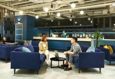 Two people talking on navy sofas in a bright breakout area with a blue reception desk in the background.