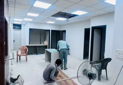 Bright open-plan workspace with a tiled ceiling, several desks, and workers installing wooden flooring.