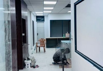 Internal view of a bright office area with dark wood wall panels and a worker fitting floor planks.