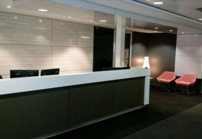 Modern reception desk with dark wood panels and pink accent chairs.