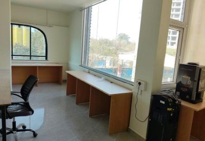 Bright coworking area with multiple wooden desks and a coffee machine station.