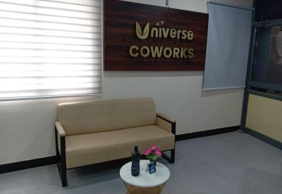 Bright lounge area with a tan sofa, branded wooden wall, and window blinds.