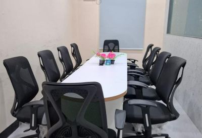 Modern conference room with an oval table, black ergonomic chairs, and a ceiling fan.