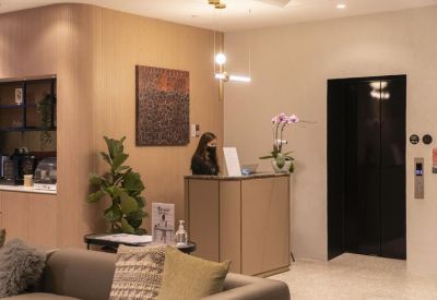 Professional reception desk with a staff member, decorative plant, and dark elevator doors.