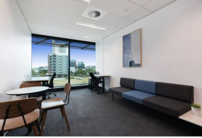 Bright office lounge with a long blue and grey sofa and city views.