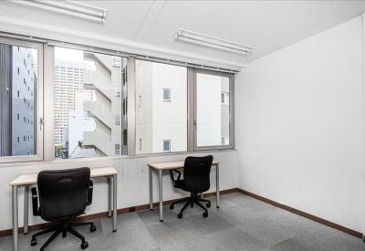 Bright private office with two desks and large windows showing city buildings.