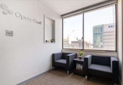 Lounge area with grey armchairs next to a large window offering city views and natural light.