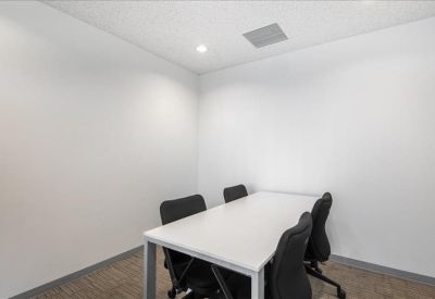 Small meeting room with a white table and four black chairs against plain white walls.