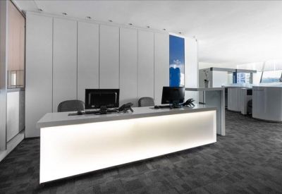 Brightly lit reception desk with a glowing white front and dark grey carpeting.