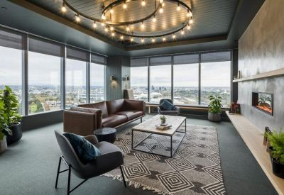 Communal lounge with a leather sofa, patterned rug, and floor-to-ceiling windows overlooking the city.