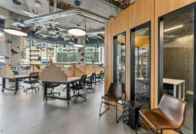 Bright coworking area with rows of desks and private glass-enclosed office pods.