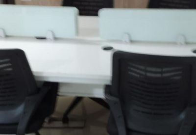 Open-plan office space with rows of white workstations and a wall-mounted television.