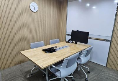 Four-person meeting room with a wooden table, wall-mounted clock, and whiteboards.