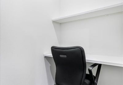 Compact private workstation with a white desk, shelf, and black office chair.