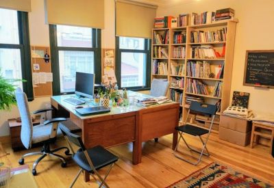 Spacious office with large wooden desks, bookshelves, and natural light from multiple windows.