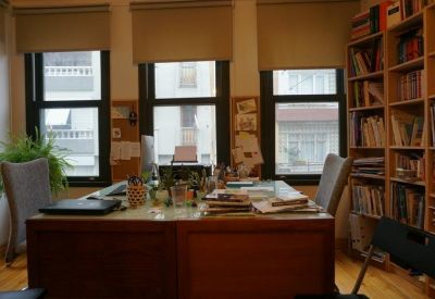 Close-up of a shared workspace desk with computer monitors and a view of neighboring buildings.
