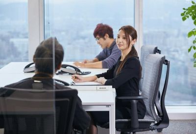 Shared office space with desks separated by glass partitions and city views.