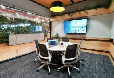 Modern meeting room with a round table, grey carpet, and a large display screen.