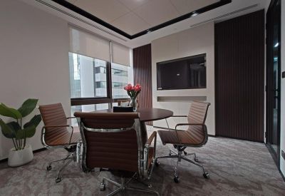 Modern meeting room with a round wooden table, tan leather chairs, and a wall-mounted television.