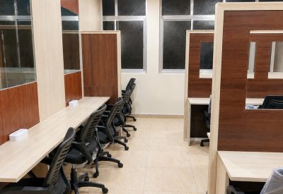 Bright open-plan workspace with multiple wooden desks, ergonomic chairs, and large windows.