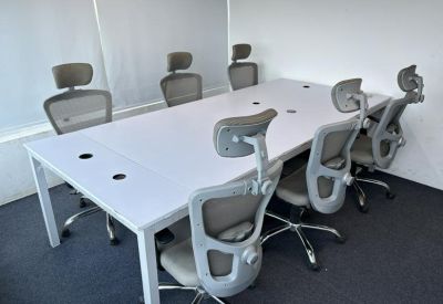 Clean white meeting table surrounded by several grey ergonomic mesh chairs.