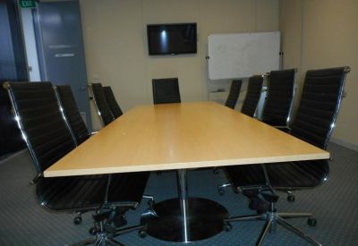 Professional boardroom with a wooden table, black leather chairs, and a whiteboard.