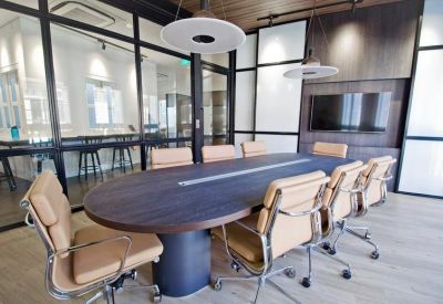Modern meeting room with a dark oval table, tan leather chairs, and glass walls.
