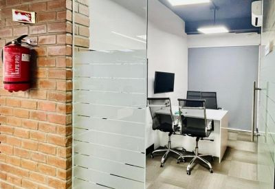 Private glass-walled office with a frosted privacy strip, white desk, and red fire extinguisher on a brick wall.