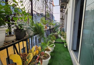 Long narrow balcony with artificial grass flooring, potted plants, and protective safety netting.
