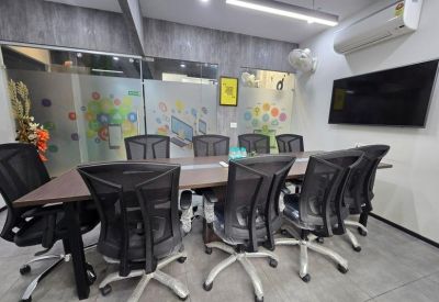 Meeting room with a long dark wood table, black mesh chairs, and a wall-mounted TV.