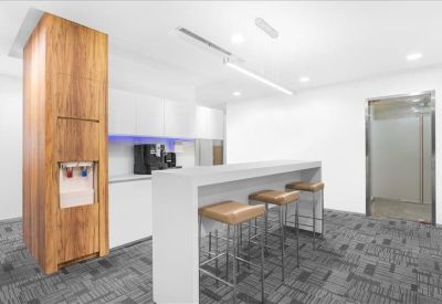 Modern breakroom area featuring a white breakfast bar, wooden cabinetry, and high stools.
