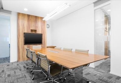 Modern boardroom with a large wooden table and wall-mounted presentation screen.