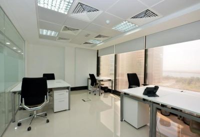 Open-plan workspace with multiple white desks and large windows with blinds.