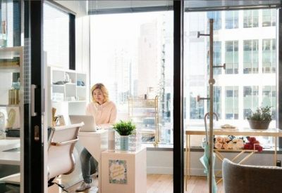 Bright glass-walled private office with a desk and city views.