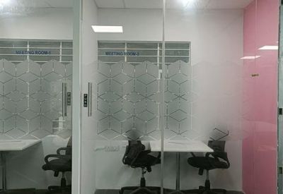 Glass-walled private office pods featuring white desks and black chairs.