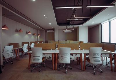 Bright open-plan office featuring rows of white desks with wooden legs and warm pendant lighting.