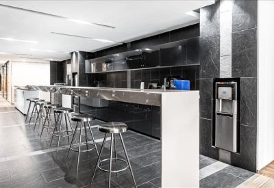 Modern office breakout area featuring a long white bar counter with chrome stools and black cabinetry.