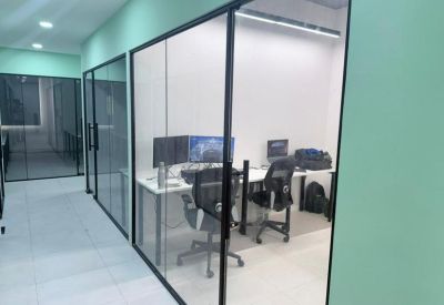 Glass-walled office corridor showing a private workspace with multiple monitors.