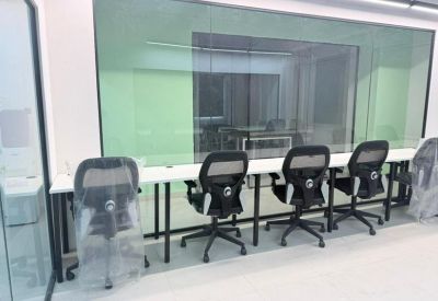 Long workstation bench with four ergonomic chairs against a large interior glass window.