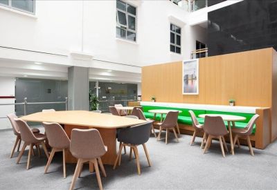 Modern communal breakout area featuring a long wooden table, green banquet seating, and vibrant orange wall.