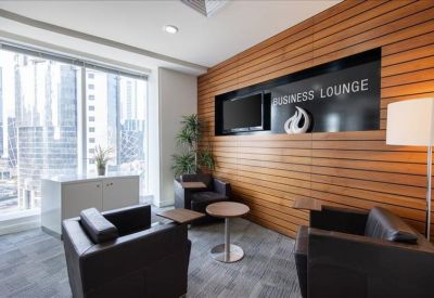 Wood-paneled business lounge with black leather armchairs and a built-in television screen.