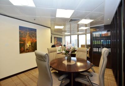Circular wooden meeting table surrounded by high-back chairs in a bright room with city views.